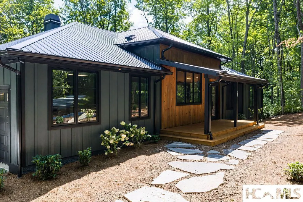 Dark board-and-batten mountain home with a standing-seam metal roof and cedar porch in the woods